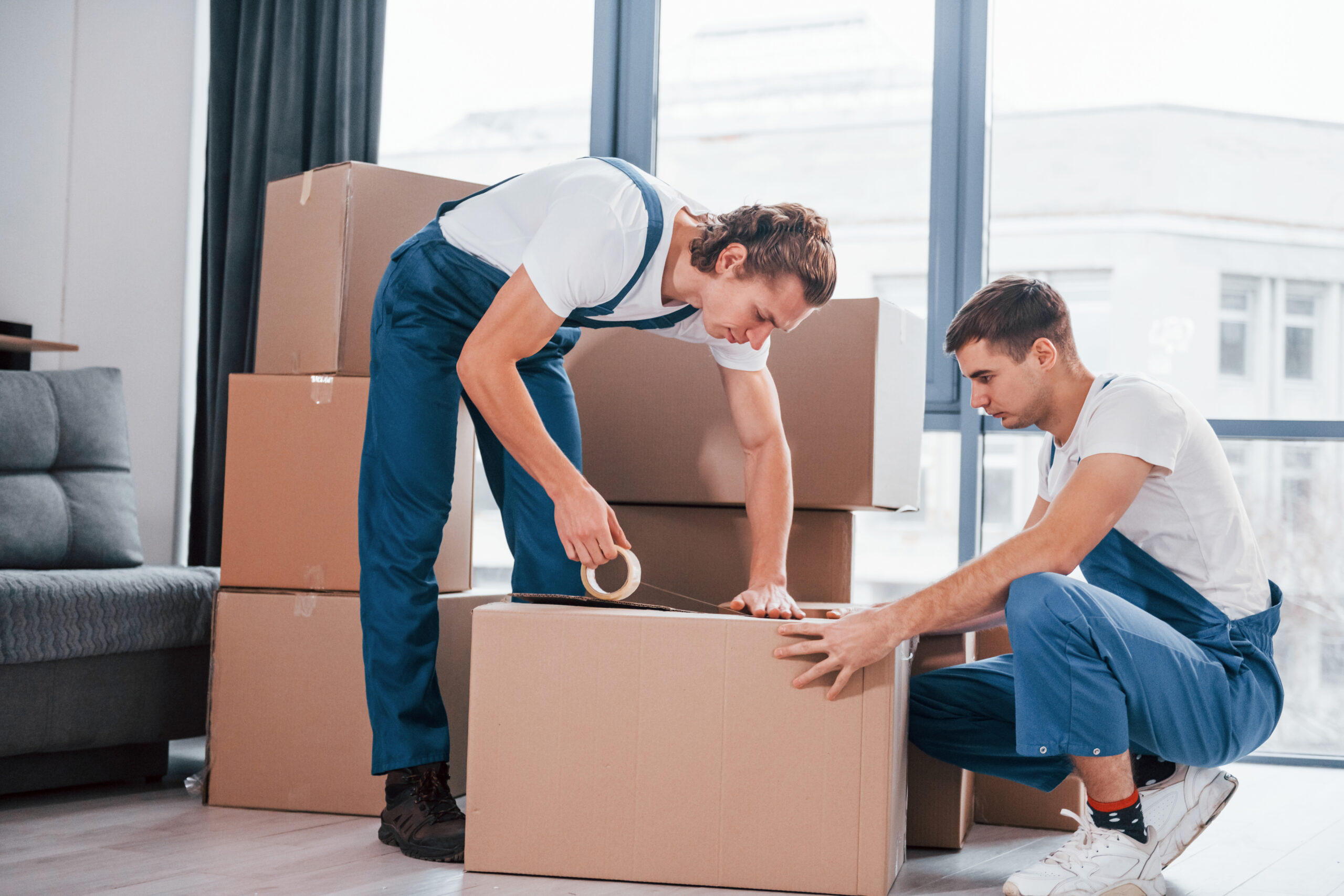 packaging the box. two young movers in blue uniform working indoors in the room